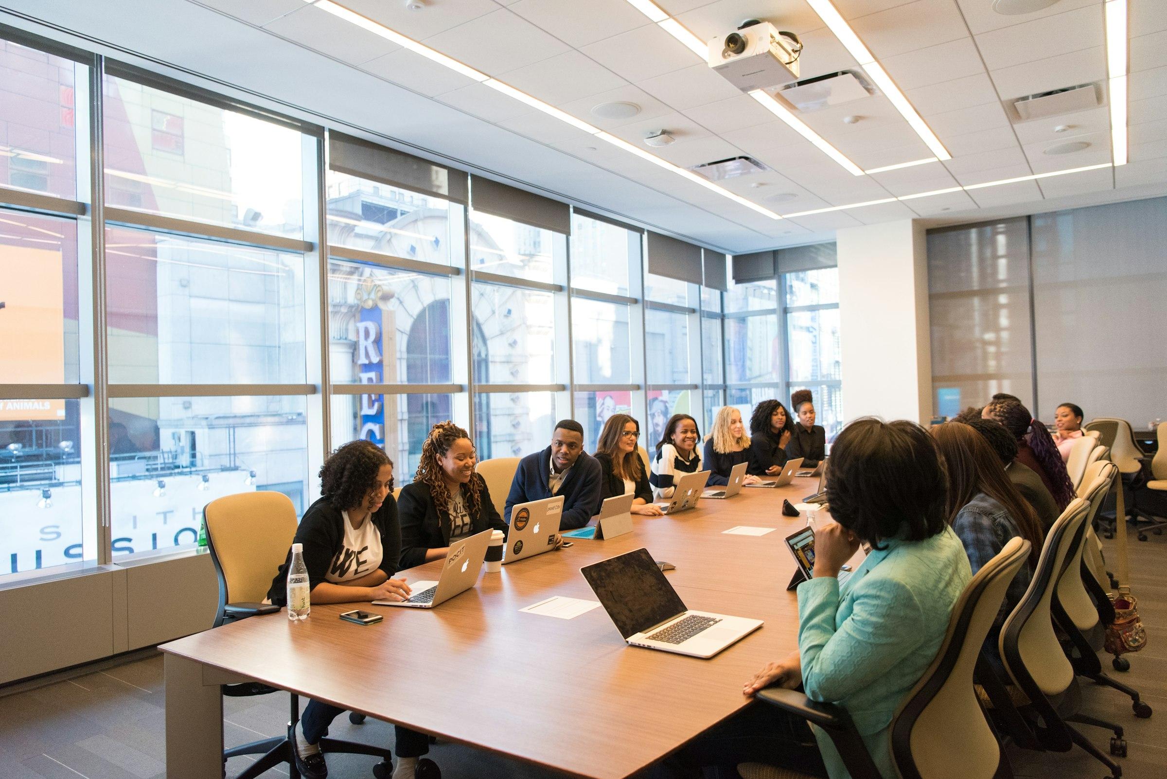 A diverse team gathered around a boardroom table with their laptops