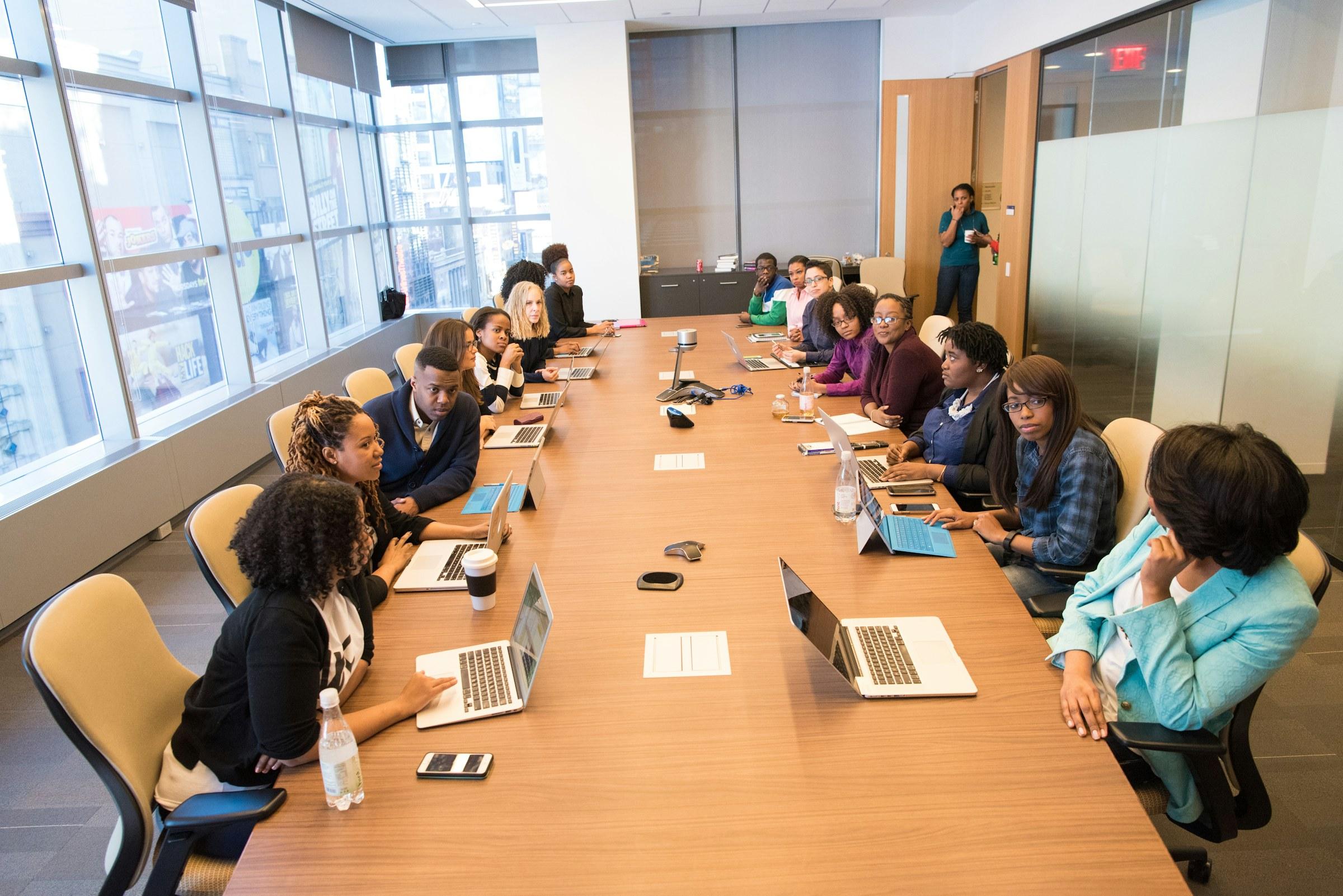 A large team gathered around a long boardroom table with laptops