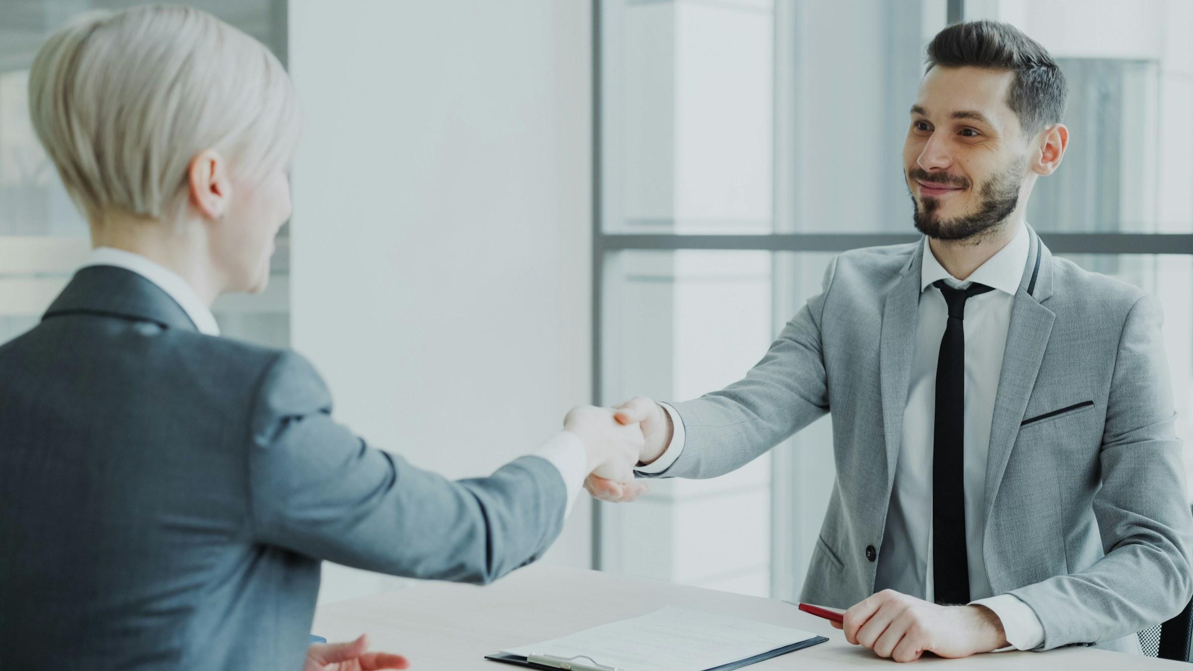 Two professionals shaking hands across an office table