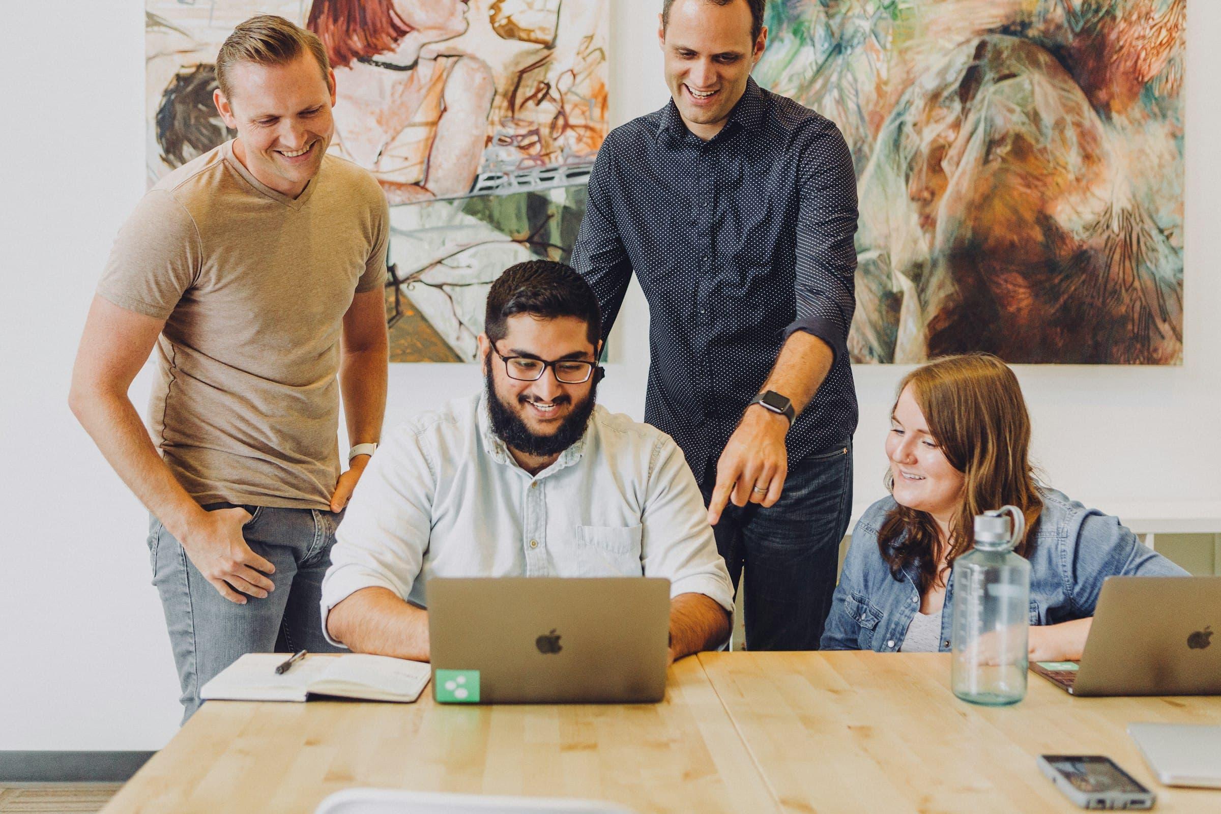 Four colleagues smiling as they review information together on a laptop